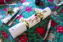 High angle close-up of cutlery and white Christmas cracker on green and red table cloth with Christmas motif. — Stock Photo