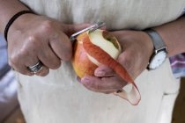 Primo piano di donna che sbuccia una mela rossa con pelapatate a doppia lama . — Foto stock