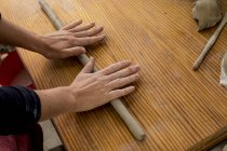 Hands of ceramic artist in workshop rolling piece of clay on wooden table. — Stock Photo