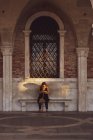 Donna seduta su panchina sotto la finestra ad arco a Venezia, Veneto, Italia . — Foto stock