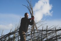 Бородатий чоловік тримає купу дерев'яних плетених під час будівництва традиційного живоплоту . — стокове фото