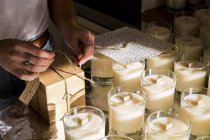 High angle close up of person wrapping handmade white jar candles. — Stock Photo