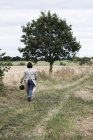 Vista trasera de la mujer caminando a lo largo del camino rural y llevando canasta de mimbre marrón
. - foto de stock
