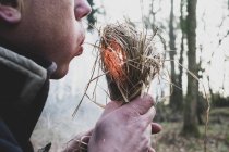 Close-up of man blowing on bundle of straw igniting fire. — Stock Photo