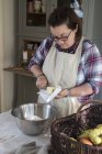 Frau in Schürze steht in Küche und schneidet Butterstücke in Metallschüssel, die mit Mehl gefüllt ist. — Stockfoto