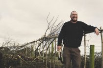 Bearded man holding axe and bill hook standing next to newly built traditional hedge and laughing. — Stock Photo