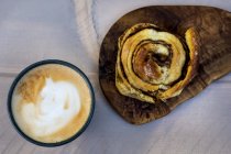 Gros plan sur un pain à la cannelle fraîchement cuit et une tasse de cappuccino . — Photo de stock