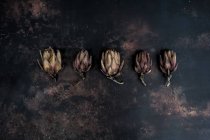 Top view of five baked artichokes on black rusty surface. — Stock Photo