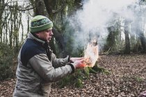 Mann steht im Wald und hält brennendes Strohbündel in der Hand, das Feuer entfacht. — Stockfoto