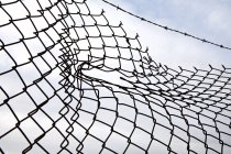 Hole in chain link fence with cloudy sky, close-up — Stock Photo