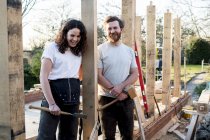 Smiling man and woman holding hand tools while standing on building site of residential building. — Stock Photo