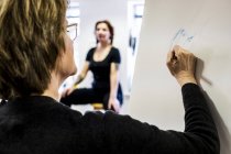 Woman standing at easel and drawing hand while model sitting in background. — Stock Photo