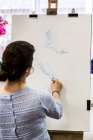 Rear view of woman standing at easel and drawing hand and foot. — Stock Photo