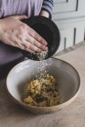 Close-up de pessoa adicionando sementes de gergelim à massa em tigela de mistura . — Fotografia de Stock