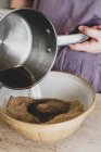 Close-up de pessoa mão derramando líquido em tigela de mistura com ingredientes de cozimento de massa . — Fotografia de Stock