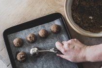 High angle close-up of person hand putting chocolate cookie dough on baking tray with scoop. — Stock Photo