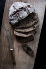 High angle view of sliced loaf of fresh brown bread on wooden board with kitchen knife — Stock Photo