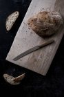 Высокий угол обзора буханки коричневого хлеба на борту с хлебным ножом — стоковое фото