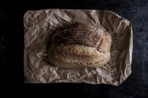 Вид сверху свежей буханки испеченного хлеба на коричневом бумажном пакете . — стоковое фото