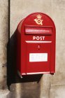 Red postbox mounted on grey city wall — Stock Photo