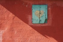 Muro rosso con finestra persiana con cuore dipinto — Foto stock