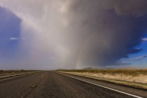 Storm and rainbow along highway road in desert — Stock Photo