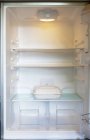 Lebensmittelcontainer im sauberen Kühlschrank mit leeren Regalen — Stockfoto