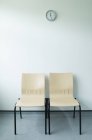 Duas cadeiras e relógio contra a parede branca — Fotografia de Stock