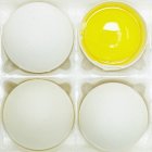 Four eggs with one cut open with yellow yolk — Stock Photo