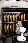 Close-up of rows of freshly smoked whole trouts in a smoker, white fan standing in front. — Stock Photo