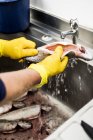 Close-up of man in yellow rubber gloves cleaning fresh trouts in metal sink. — Stock Photo