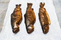 High angle close-up of three fresh smoked whole trouts on white paper. — Stock Photo