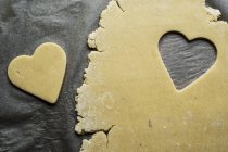 High angle close-up of heart-shaped cookies cut out of cookie dough on grey background. — Stock Photo