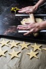 High angle close-up of male cook rolling dough for star-shaped cookies using guide rods to maintain even thickness of dough. — Stock Photo