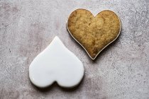 Primer plano de ángulo alto de dos galletas recién horneadas en forma de corazón decoradas con glaseado blanco . - foto de stock