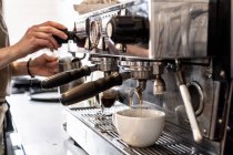 Close-up of hands of female barista making cappuccino using commercial coffee machine. — Stock Photo
