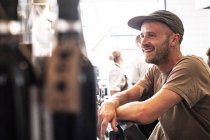 Portrait of bearded man in baseball cap standing in cafe and smiling. — Stock Photo