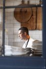 Portrait of male chef standing in commercial kitchen behind window. — Stock Photo