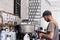 Junger männlicher Barista arbeitet mit Kaffeemaschine im Café. — Stockfoto