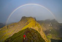 Mann klettert in Richtung Regenbogen auf den erhabenen Inseln, Norwegen, Europa. — Stockfoto