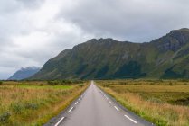 Estrada reta através de montanhas na paisagem em Lofoten Islands, Noruega, Europa . — Fotografia de Stock