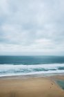 Ocean waves crashing onto sandy beach under cloudy sky, Cornwall, England, United Kingdom. — Stock Photo
