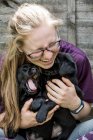 Blonde woman wearing glasses hugging two black labrador puppies. — Stock Photo