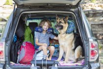 Junge im Grundalter mit Schäferhund und Reisekissen im Rücken eines Geländewagens. — Stockfoto
