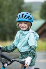 Retrato de menino de idade elementar vestindo casaco de chuva e capacete straddling bicicleta . — Fotografia de Stock