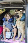 Elementary age boy with German Shepherd dog wearing travel pillows in back of  SUV. — Stock Photo