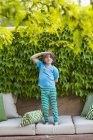 Elementary age standing on sofa pillows in front of green leaves. — Stock Photo