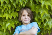 Elementary age boy standing in front of green leaves. — Stock Photo