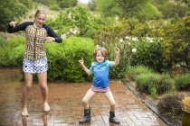 Elementary age boy with teenage sister dancing in rain. — Stock Photo