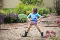Niño de edad elemental en wellingtons de pie con las manos en las caderas en el jardín . - foto de stock